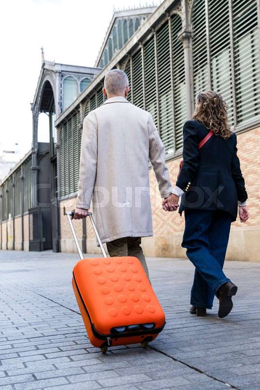 Lovely mid adult tourists couple travelling together walking old town with a suitcase. Romantic senior man and woman walking in a european city in a weekend trip.