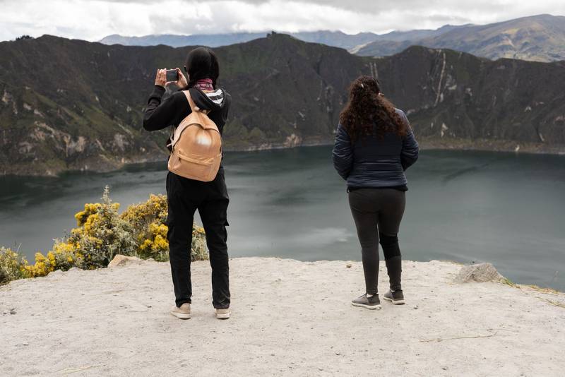 Two women stand side by side on a cliff overlooking a breathtaking landscape