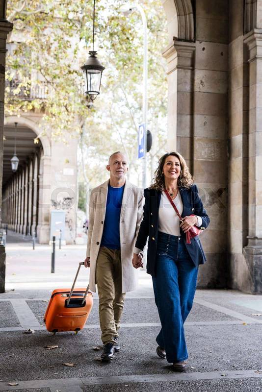 Carefree mid adult tourist couple travelling together visiting Europe city carrying luggage. Laughing senior husband and wife having fun in a weekend romantic trip.