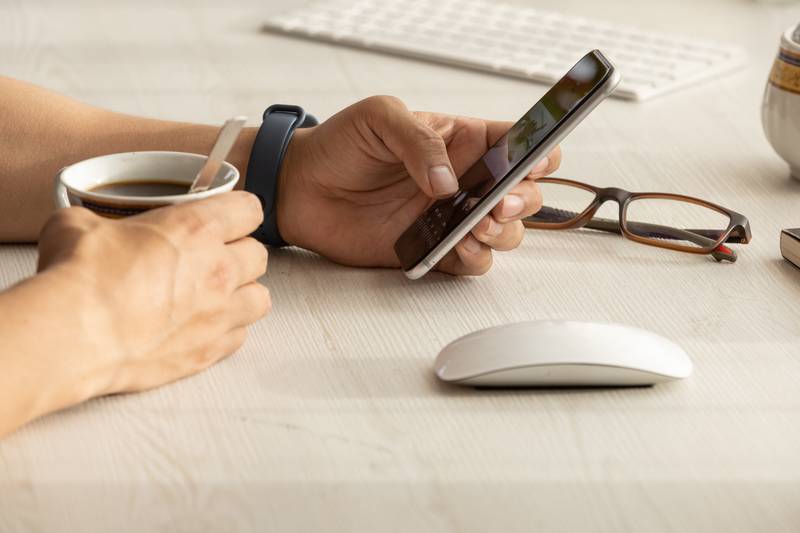 person working at his desk, detail of his hands holding a cell phone