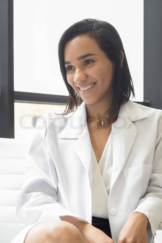 latin female doctor with short hair sitting, smiling and wearing her white uniform coat