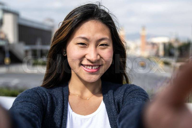 Happy handsome woman smiling relaxed and looking at camera in the street taking a selfie. Relaxed happy lady laughing and staring and holding the camera standing outdoors.