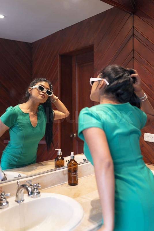 latin young woman with long black hair, wear sunglasses and green dress getting ready