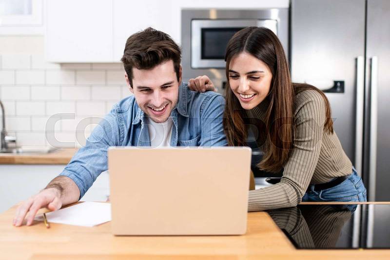 young couple planning vacations together at home looking a laptop. two cheerful young adults sitting on the kitchen. finance concept