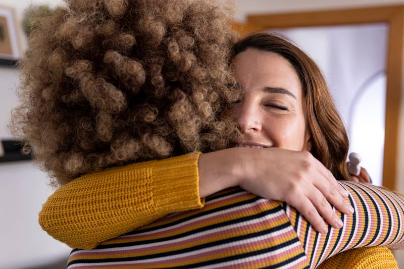 Carefree and joyful female couple hugging each other at home. Head shot close up happy multiracial girl cuddling smiling female friend. Friendship concept.