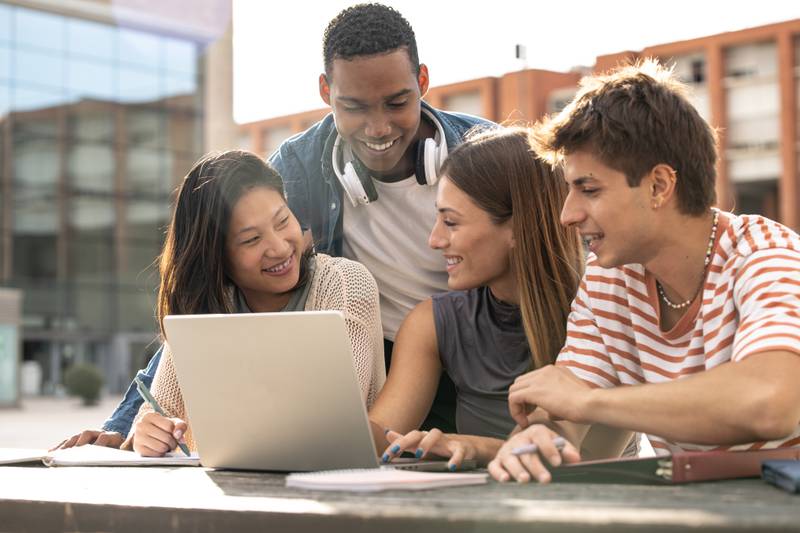 Multicultural group of people working together with a laptop.Young happy friends studying outside using computer and notes.