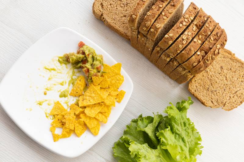 mold of sliced whole wheat bread next to a lettuce and a plate with nachos and guacamole