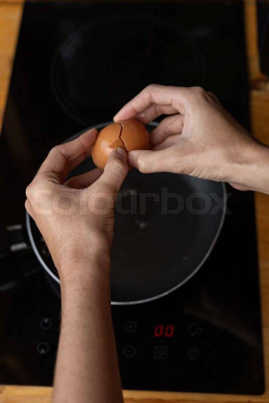 hands breaking an egg into a sizzling frying pan