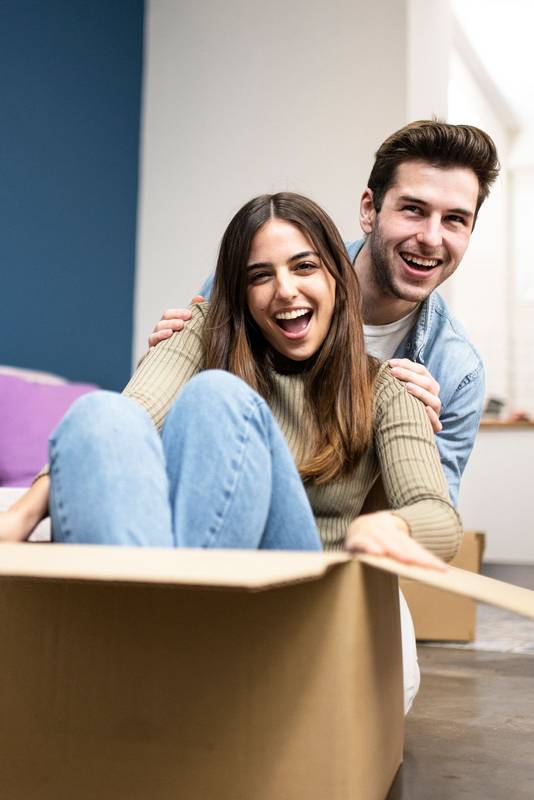 happy couple is having fun with boxes in new house at moving day. Funny friends enjoying together in his new apartment