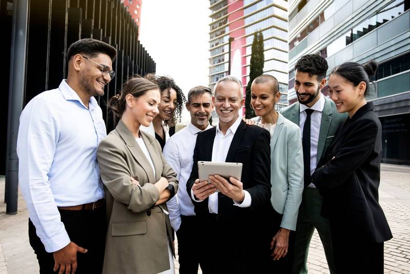 Group of successful multiracial corporate business team looking at tablet in the financial district. Smiling multiethnic professional employees company staff with older executive leader.
