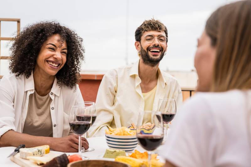 Diverse young people sitting at a terrace table having fun. Cheerful group of friends laughing and chatting while having drinks outdoors.