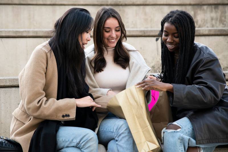three multiracial happy beautiful friends looking inside a shopping bag . Cheerful friends having fun together outdoors. Friendship concept