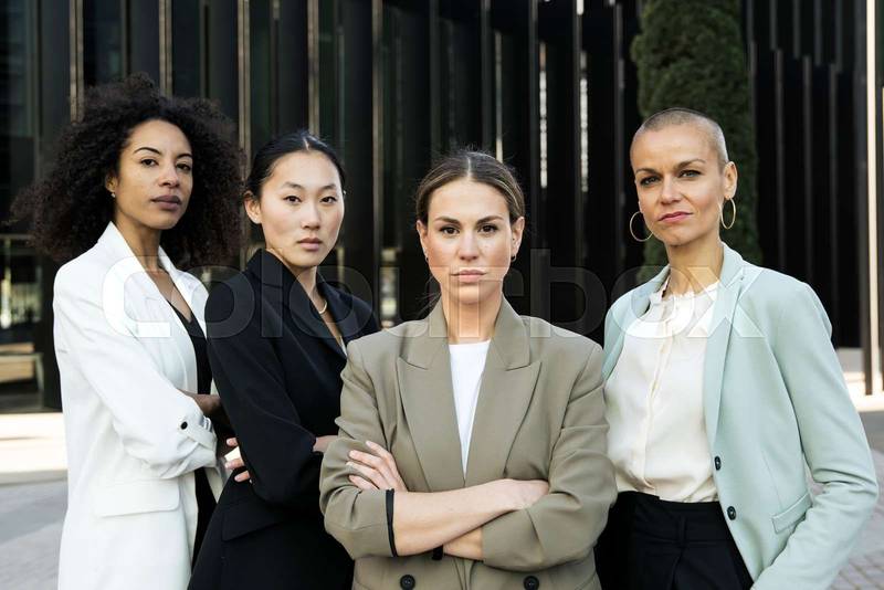 Group of confident and ambitious businesswomen looking at camera outside. Team of young successful determined executive females and staring at camera in the street.