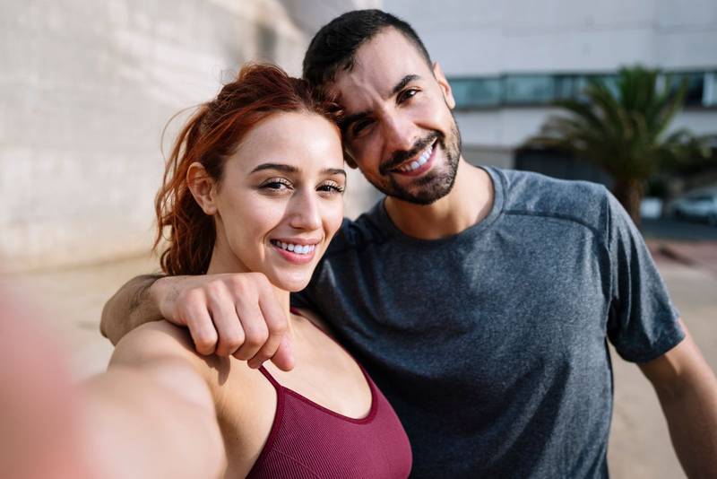 Young fit couple taking selfie smiling after training running outside. Sports lovely joyful active fitness friends standing taking a picture outdoors.