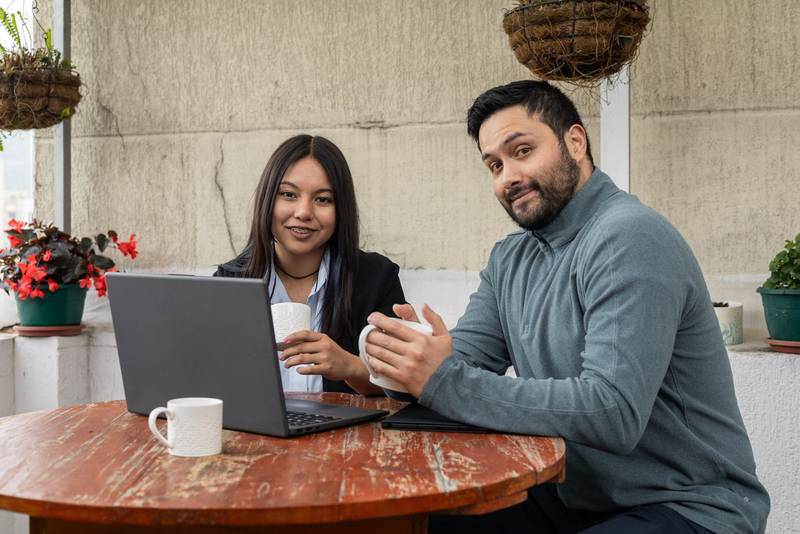 oworkers smiling while working on laptops and drinking coffee in a relaxed outdoor workspace