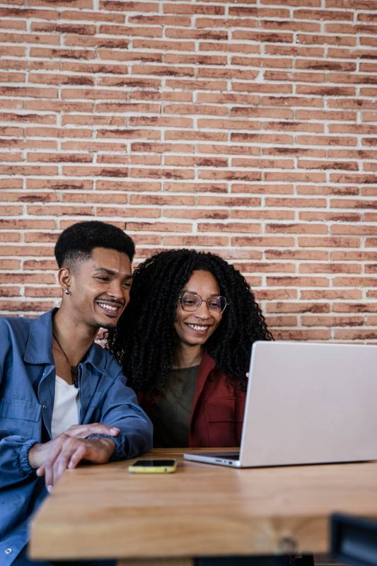 Friendly young adult woman and man in love watching at the computer screen. Happy young diverse couple sitting at living room having laptop video call at home. 