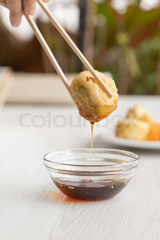 holding a timed sushi roll with wooden chopsticks while dipping it in sauce,