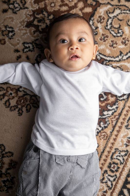lying on a textured rug in a studio, wearing shorts and a white bodysuit baby