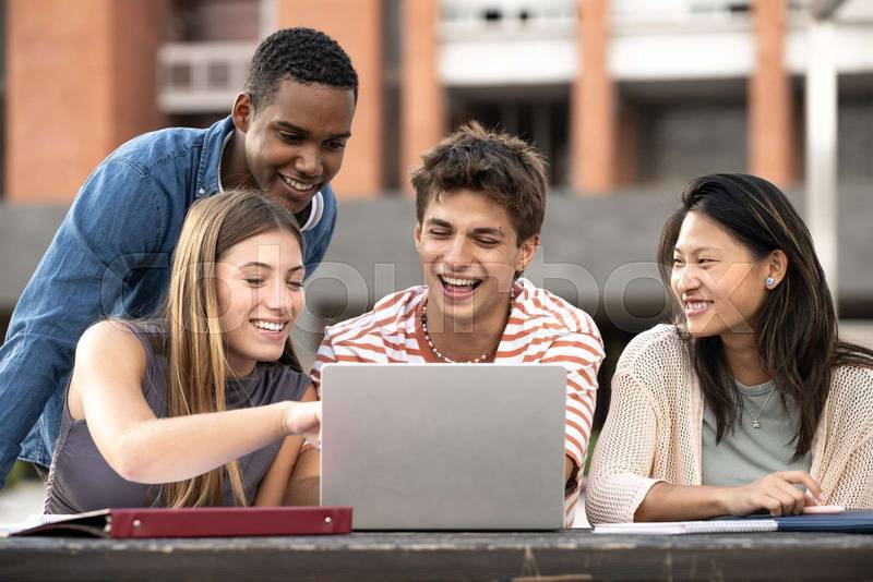 Multicultural group of people working together with a laptop.Young happy friends studying outside using computer and notes.