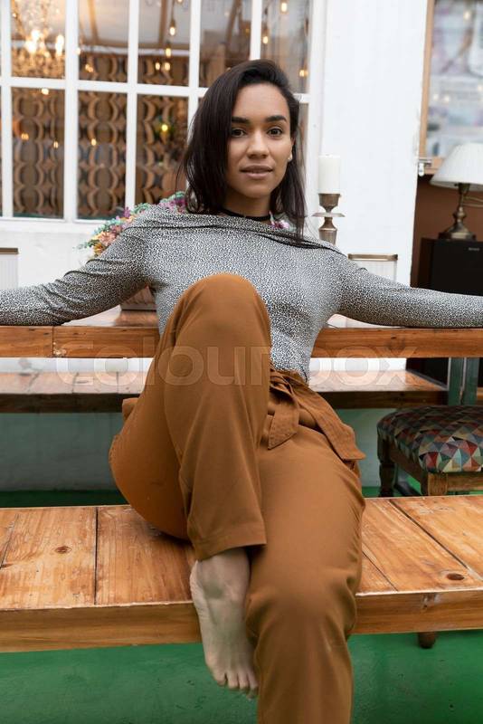 sitting on a wooden bench, wears comfortable clothes and is barefoot, fashion and modern lifestyle