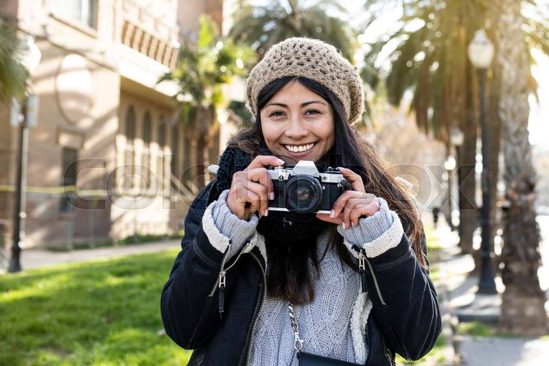 smiling woman traveler holding a camera at the city in holidays - relaxation, tourism concept