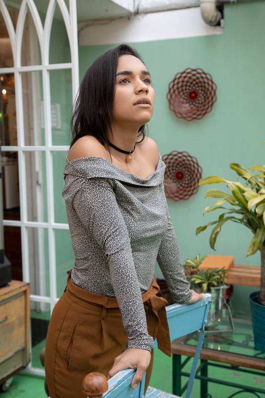 woman standing leaning on chairs, wearing casual clothes, she is inside a room decorated in a colorful