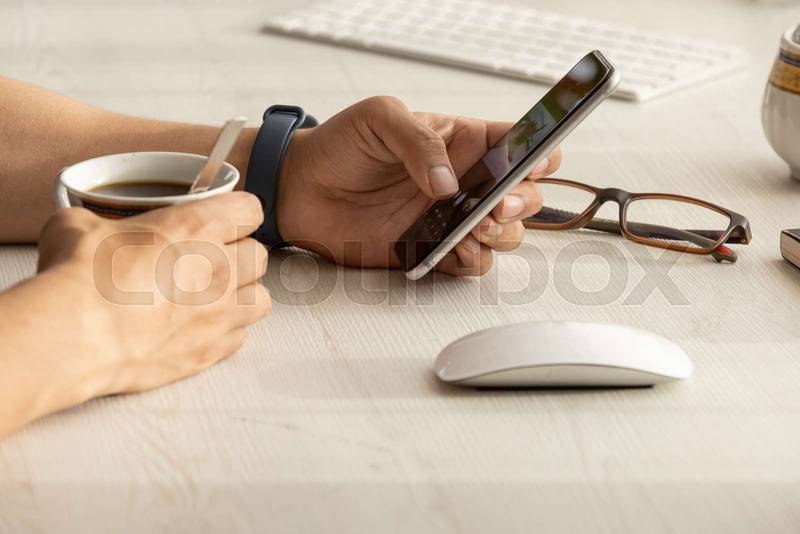 person working at his desk, detail of his hands holding a cell phone