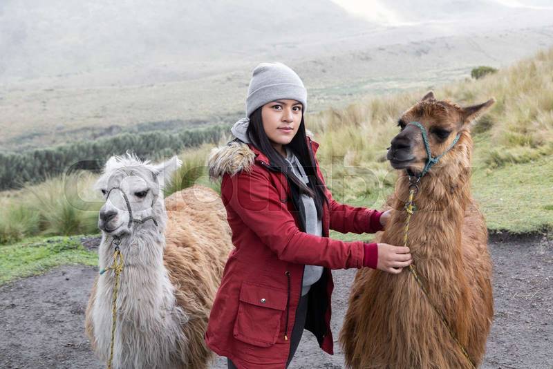 rural destination with young woman wearing a winter clothes while walking with some llamas