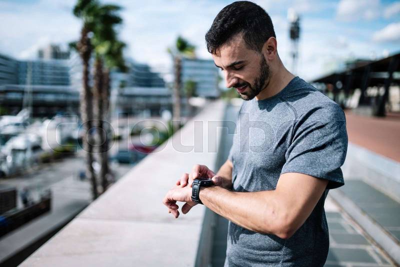 Active man looking swatch during exercise outside. Fitness male looking his smartwatch checking running time after cardio training. 
