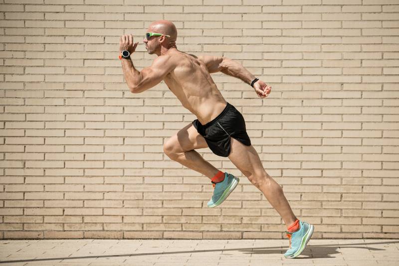 Sideview of a fit athlete running in the street without shirt. Muscular man trainning and sprinting in a city.