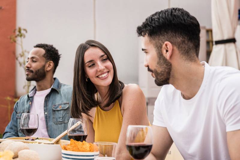 Young beautiful woman smiling to handsome man in a dinner party. Confident lady talking with young guy while sitting and eating in a terrace.