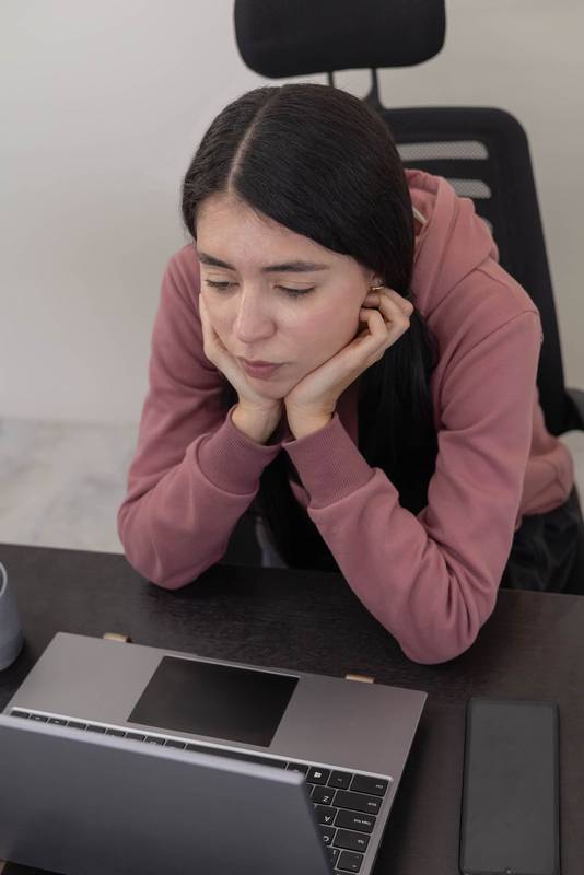 professional woman stares at her laptop screen with a bored expression, feeling disengaged and tired while completing office tasks