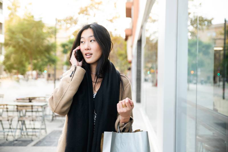 Young woman at the street with shopping bags talking on mobile phone