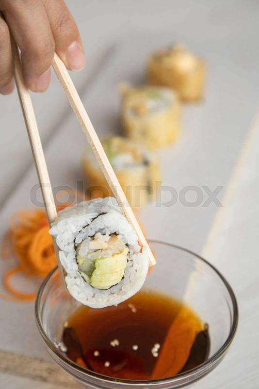 appetizers plate, wooden chopsticks holding a sushi roll with rice, healthy