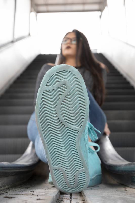 young woman with long black hair sitting on the railing showing the sole of her shoe
