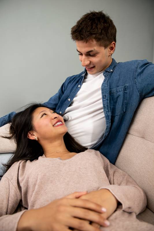 Affectionate relaxed couple staring each other sitting comfortable at their living room. Cozy smiling boyfriend looking his girlfriend enjoying carefree leisure weekend time at a home.