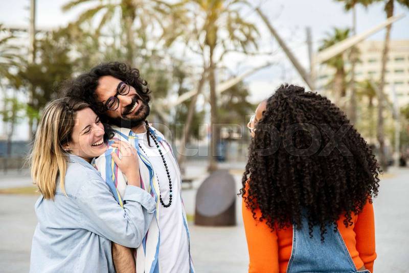Lovely young couple laughing with a friend in the street. Three diverse people smiling, having fun and looking at each other outside.