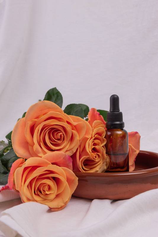 dropper with oil extract in a bowl next to roses, natural cosmetic product