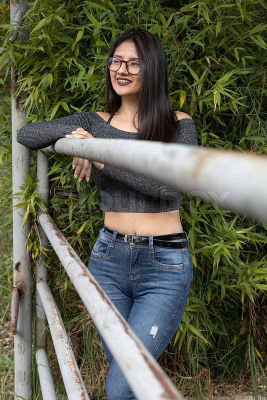latin woman with straight black hair wearing glasses, jeans and a gray casual buso
