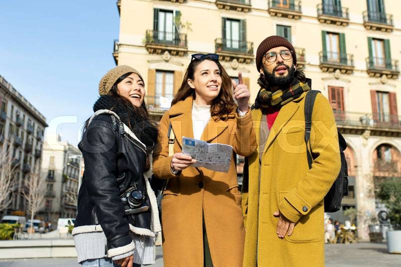 Group of tourists looking a map walking on the street. Three cheerful friends seraching a monument during a city travel