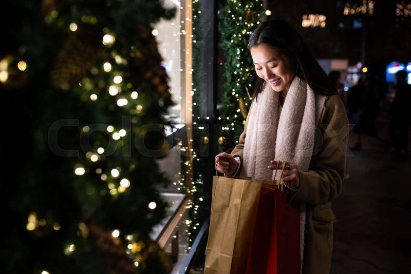 Satisfied young lady looking inside shopping bags in the street. Happy female holding shopping bags in Christmas.