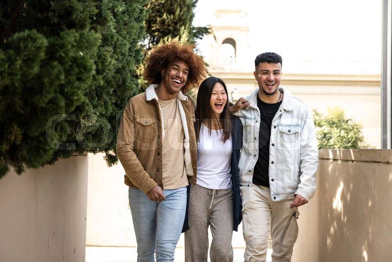 Three happy young people smiling and looking relaxed walking in the street.Multiracial group having fun and hugging each other walking in the park.