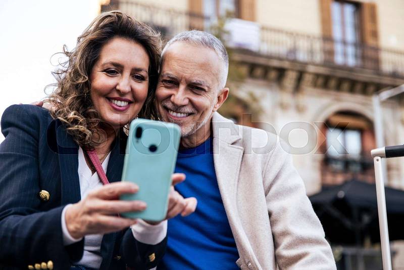 Cheerful mid adult couple having fun together taking a selfie in the street. Romantic senior couple smiling taking picture together in european city.