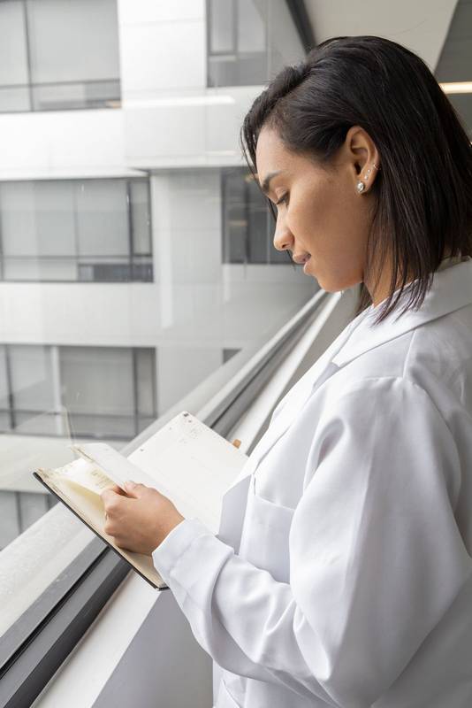 female doctor reading a book by a window in the daytime
