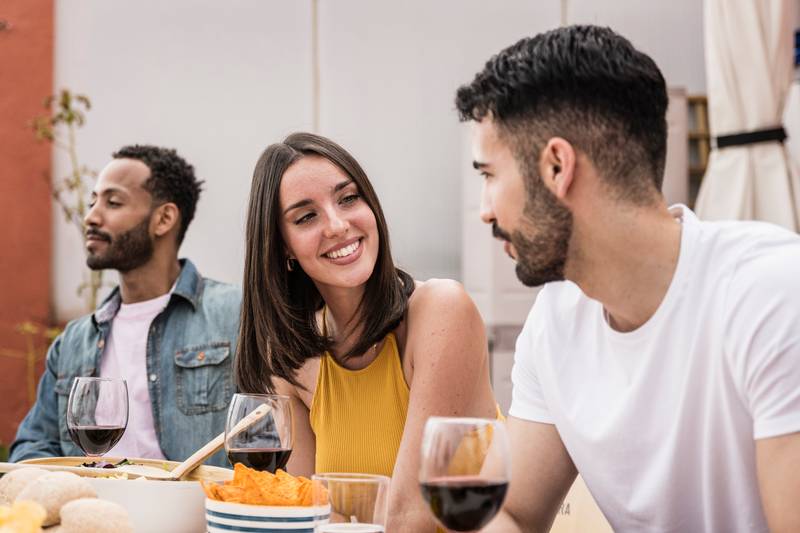 Young beautiful woman smiling to handsome man in a dinner party. Confident lady talking with young guy while sitting and eating in a terrace.