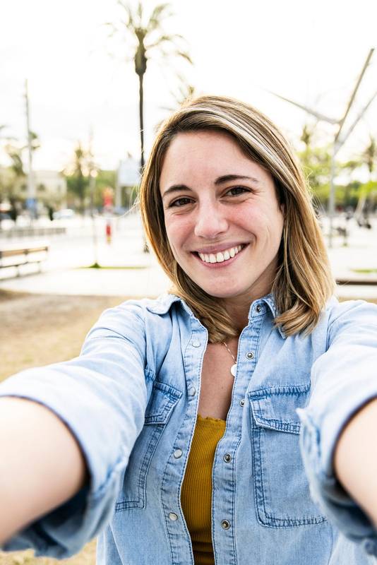 Vertical picture of a gorgeous cheerful blond hair female carefree and satisfied taking a selfie outside. Handsome happy young woman smiling and looking at camera in the street.