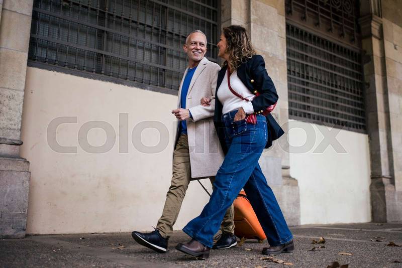 Affectionate mid adult tourist couple travelling together smiling looking each other. Cheerful senior man and woman walking in a city in a weekend romantic trip