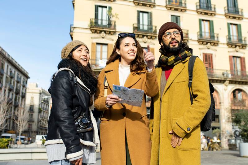 Group of tourists looking a map walking on the street. Three cheerful friends seraching a monument during a city travel