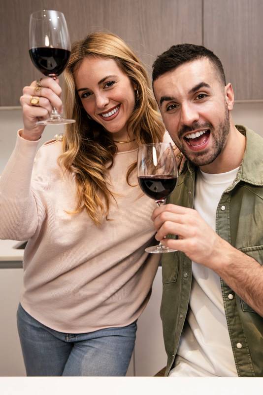 Affectionate joyful couple celebrating toasting with wine in kitchen. Happy smiling man and woman drinking with glasses in home.