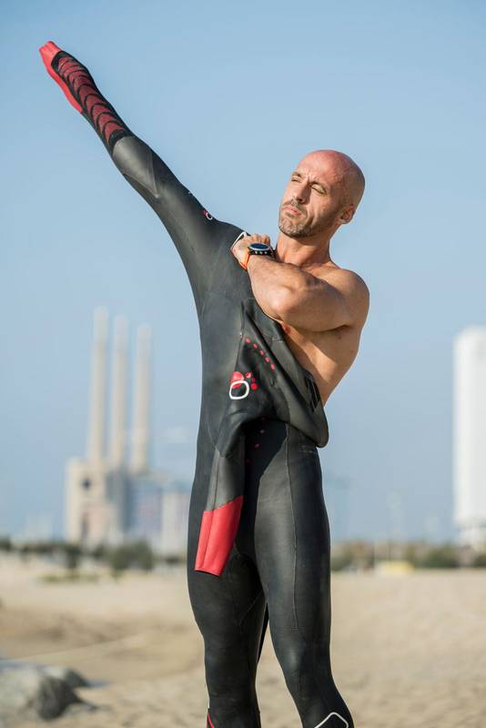 Male swimmer getting ready for swim training in the beach with urban background. Confident man putting on a wetsuit to go swimming in the ocean.